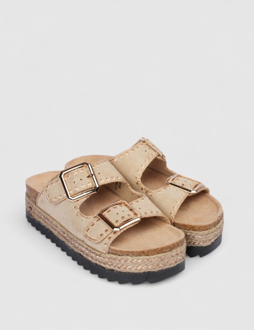 Cette image contient Mules en suédine beige avec boucles dorées chez Joliesse. à 0,00 TND en Tunisie. L'hexa de l'arrière plan e