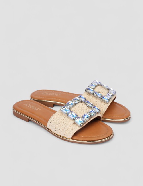 Cette image contient Mules plates en tissu beige avec boucle bijou chez Joliesse. à 0,00 TND en Tunisie. L'hexa de l'arrière pla
