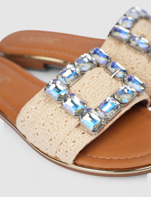 Cette image contient Mules plates en tissu beige avec boucle bijou chez Joliesse. à 0,00 TND en Tunisie. L'hexa de l'arrière pla